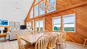 A spacious dining area with a long wooden table and chairs, large windows offering a view of the beach, and a cozy seating area with a fireplace. - To the Beach and Back at Salvo 5 Bedroom Home with a Private Pool, Spa and Near Beach Access! (Salvo)