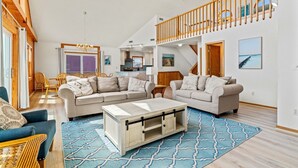 A spacious living area with a large sofa, a coffee table, and a dining table. There is a staircase leading to an upper level. - To the Beach and Back at Salvo 5 Bedroom Home with a Private Pool, Spa and Near Beach Access! (Salvo)