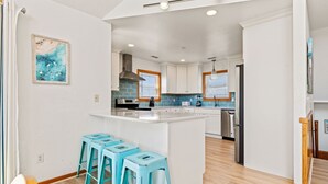 A modern kitchen with white cabinets, a central island, and blue bar stools. - To the Beach and Back at Salvo 5 Bedroom Home with a Private Pool, Spa and Near Beach Access! (Salvo)