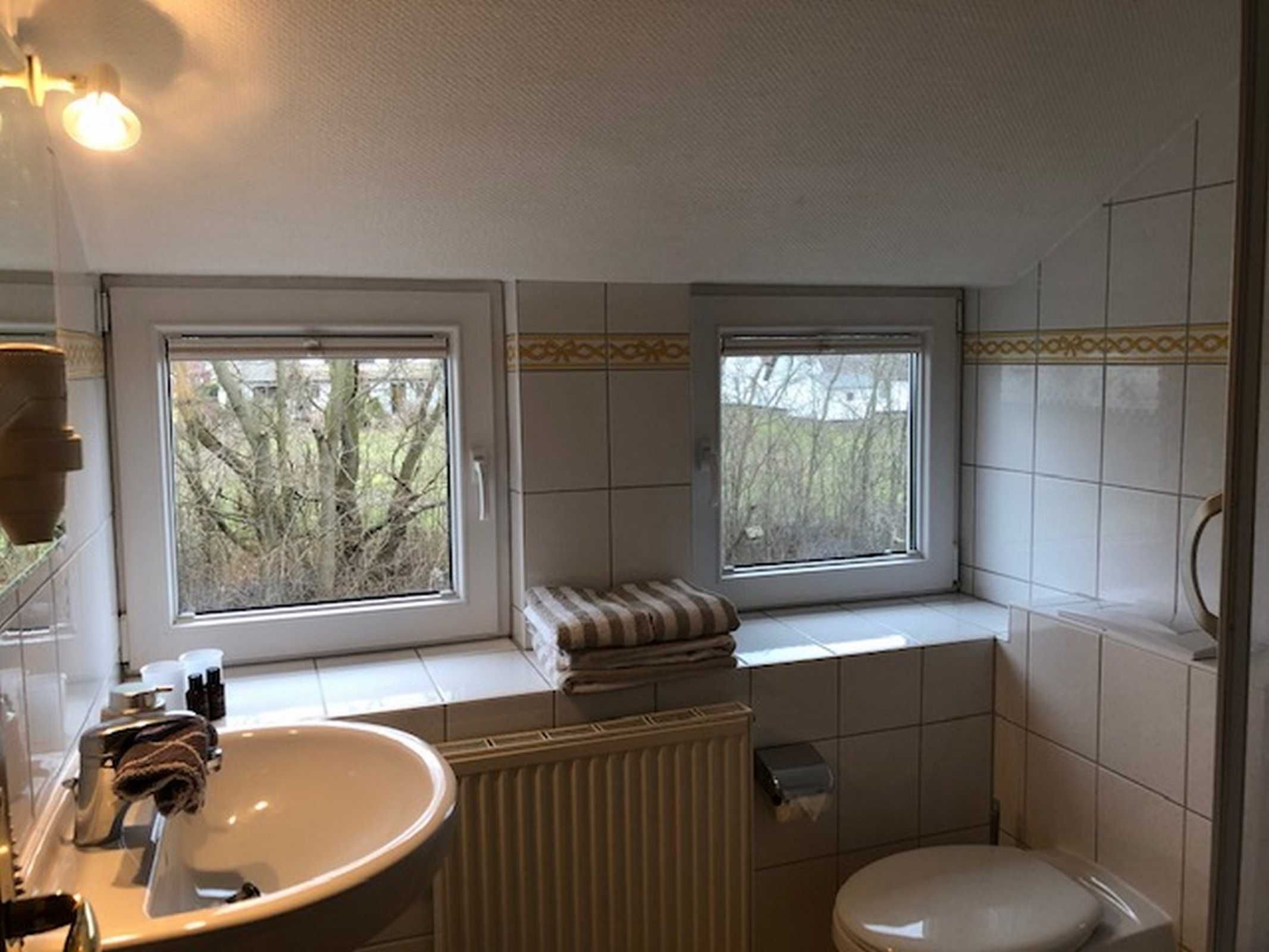 Ein Badezimmer mit Fenster, Waschbecken, Toilette und Heizkörper.