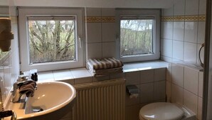 A bathroom with a window, a sink, a toilet, and a radiator.