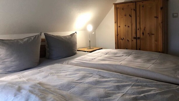 A bedroom with a bed, two pillows, a nightstand, a lamp, and a wooden wardrobe.