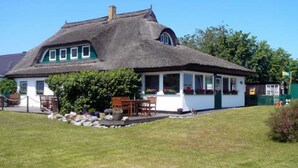 A traditional thatched-roof house with a porch, a small garden, and a clear blue sky.
