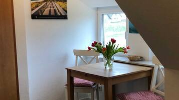 Ein Essbereich mit einem Holztisch und Stühlen, einer Vase mit roten Blumen und einem Fenster mit Blick auf Grünflächen.