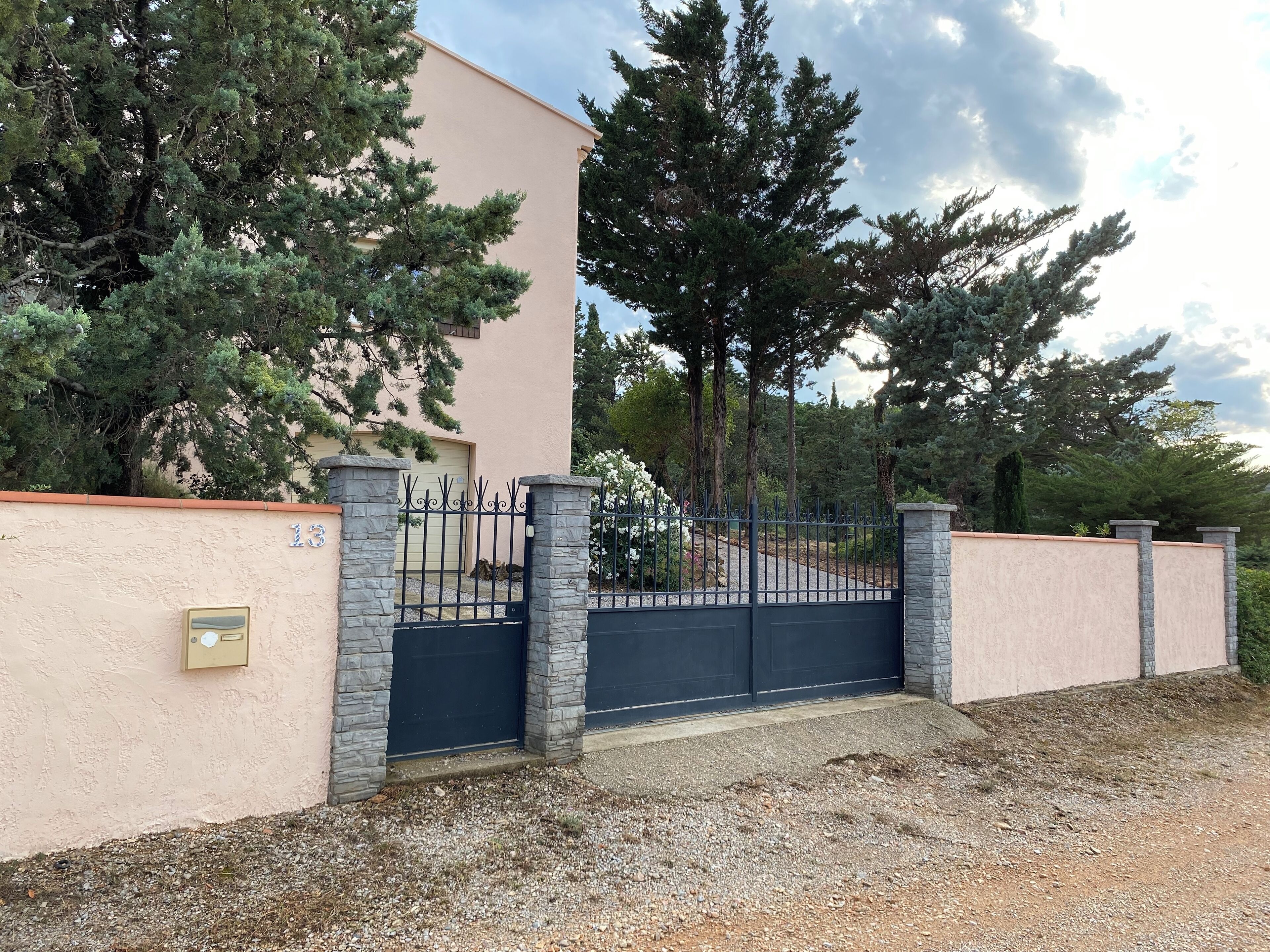Propiedad resguardada por un muro, con fachada color beige, pilares de piedra y una puerta negra.