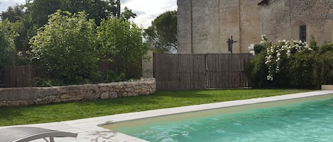 A swimming pool with a stone wall and a wooden fence in the background.
