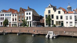 A canal with a row of traditional European buildings, a small boat docked at the canal's edge, and a clear blue sky. - Middelburg4you (Middelburg)