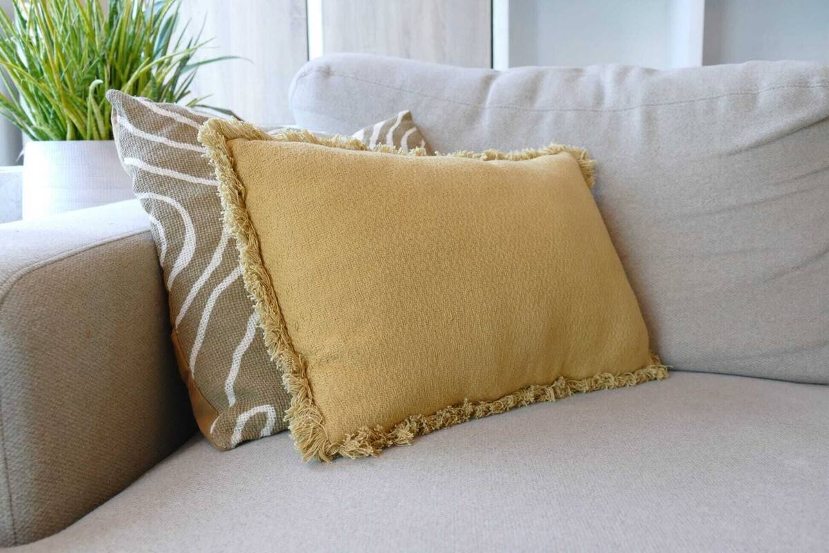 A beige sofa with two pillows, one plain and one with a striped pattern.