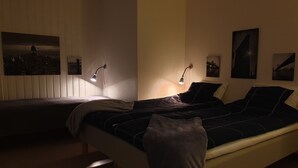 Une chambre à coucher faiblement éclairée, avec un lit, deux lampes de chevet et une œuvre d’art représentant un paysage urbain accrochée au mur.