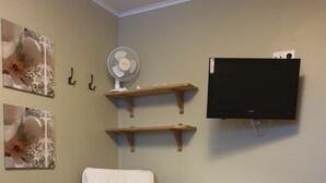 Une pièce comprenant une chaise en bois, une petite table, un téléviseur fixé au mur et deux étagères en bois.