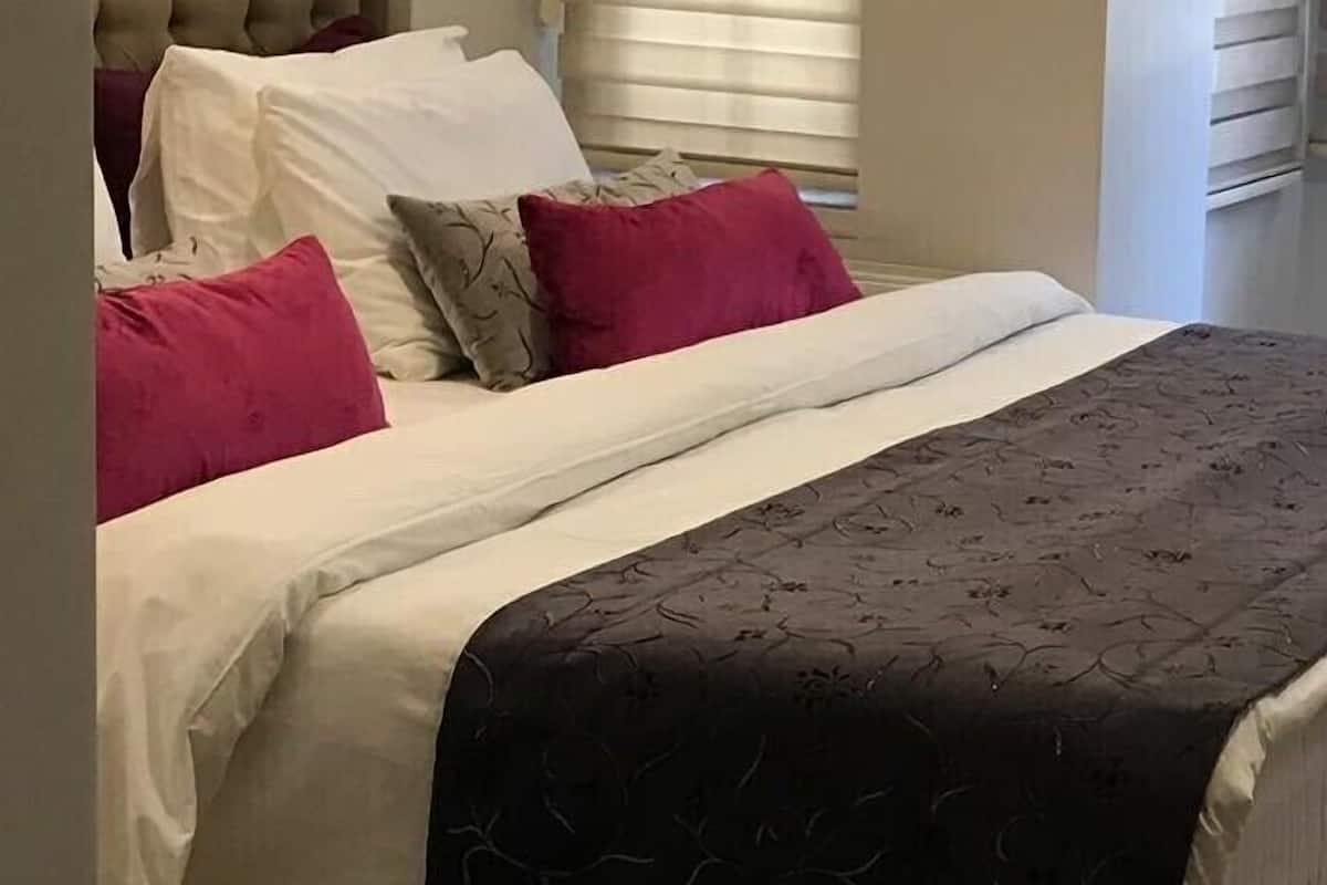Un lit bien fait, avec une literie blanche et marron foncé, agrémentée d’un plaid à motifs.
