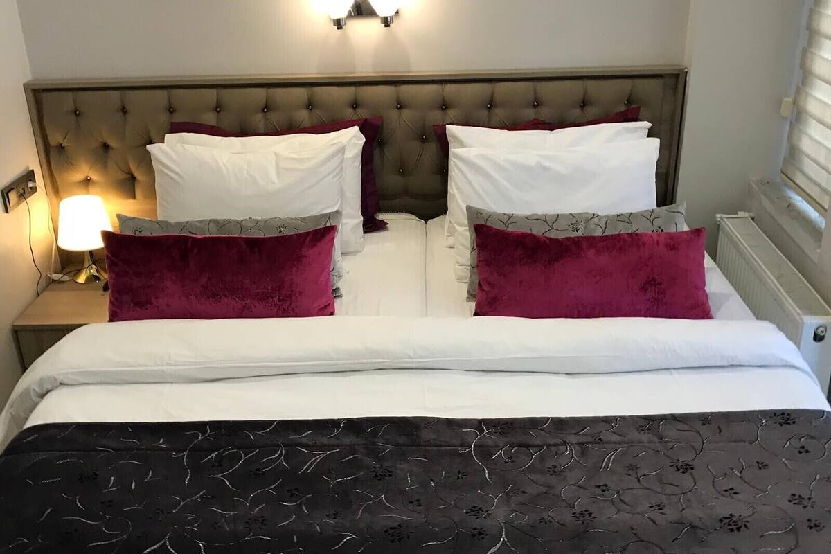 Un lit bien fait, avec des oreillers blancs et bordeaux, une couvre-lit à motifs sombres et une tête de lit capitonnée.