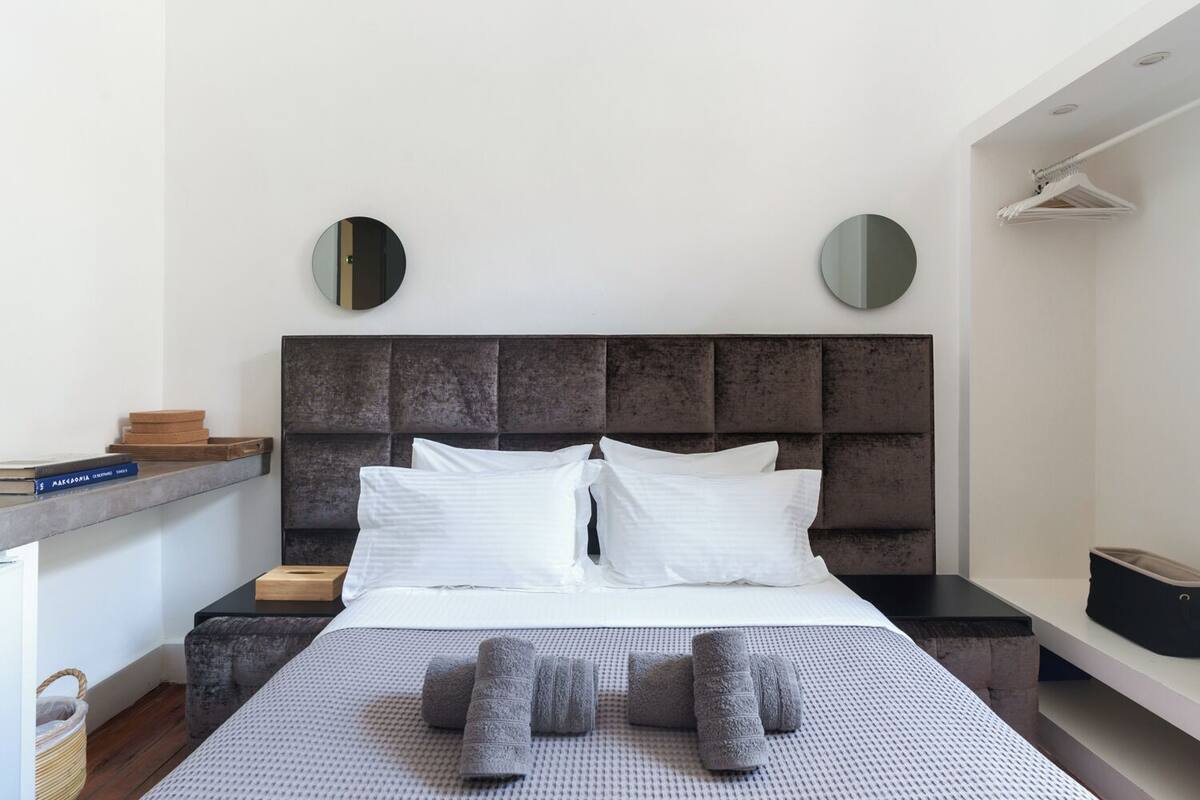 A modern bedroom with a large bed, two bedside tables, a headboard, and two wall-mounted mirrors.