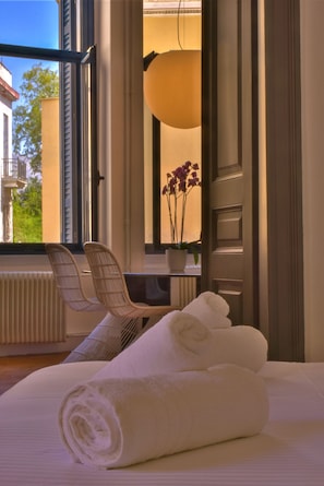 Quarto de hotel com cama, cadeira, janela com vista para vegetação e planta em vaso.
