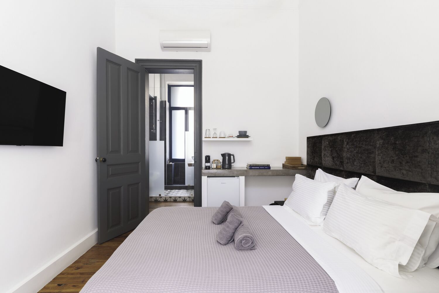 A bedroom with a bed, pillows, a bedside table, a TV, and a door leading to a bathroom.