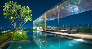 Una piscina infinita con piso de vidrio, sillas de descanso y un árbol.