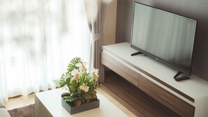 A modern living room with a flat-screen TV on a wooden console, a white sofa, and a decorative plant on a white coffee table. - The Astra Condo (Chiang Mai)