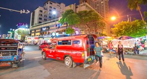 Un tuk-tuk rojo estacionado en una calle concurrida con una fachada de tienda al fondo.