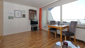 Una sala de estar con piso de madera, una mesa de comedor con sillas, un televisor y un aparador.