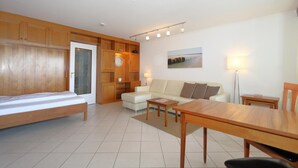 A modern living room with a sofa, a dining table, and a wooden cabinet. - Haus am Meer14-app 091 WB (Sylt)