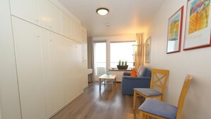 A room with a sofa, chairs, a table, and a large wardrobe.