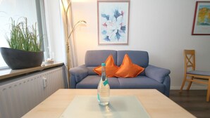 A living room with a sofa, a table with a bottle, a plant, and a framed picture on the wall.