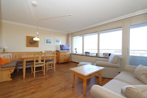 Ein gemütliches Wohnzimmer mit Esstisch aus Holz, einer Couch und einem Fernseher.