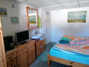 Een slaapkamer met een bed, een televisie op een houten dressoir, een wastafel en een deur die naar een andere kamer leidt.