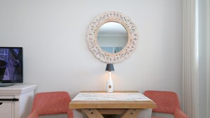 Une petite pièce agréable et chaleureuse, avec un bureau blanc, deux chaises roses, une table en bois, un miroir décoratif et une lampe.