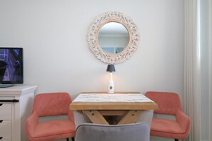 Ett litet, ombonat rum med ett vitt skrivbord, två rosa stolar, ett träbord, en dekorativ spegel och en lampa.