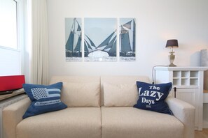 A beige sofa with two pillows, one with a flag design and the other with text. There are three framed pictures on the wall above the sofa.
