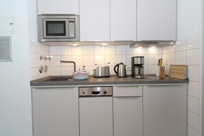 A modern kitchen with white cabinets, a stainless steel microwave, a coffee maker, and a toaster.