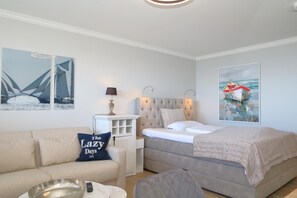 A bedroom with a bed, a nightstand, a lamp, a sofa, and two paintings on the wall. - House by the sea 034 Wb, Germany (Sylt)