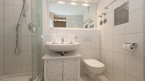 Une salle de bain moderne avec une douche à parois de verre, un lavabo blanc agrémenté d’un meuble décoratif, des toilettes et un miroir au-dessus du lavabo.