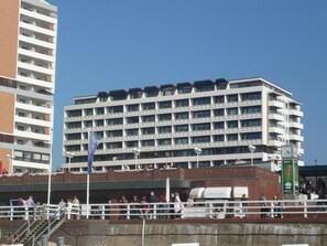 A multi-story hotel with a modern architectural design, featuring balconies and a prominent clock tower.
