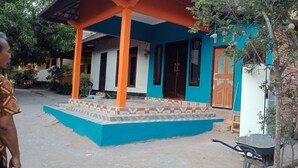 A house with a blue and orange exterior, a tiled porch, and a wheelbarrow near the entrance. - T&T Homestay (Kuta)