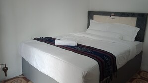 A neatly made bed with white linens and a patterned throw blanket. - T&T Homestay (Kuta)
