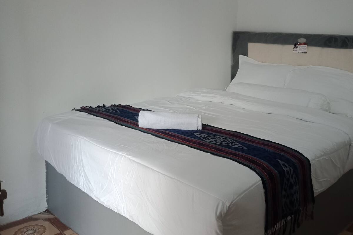 A neatly made bed with white linens and a patterned throw blanket.
