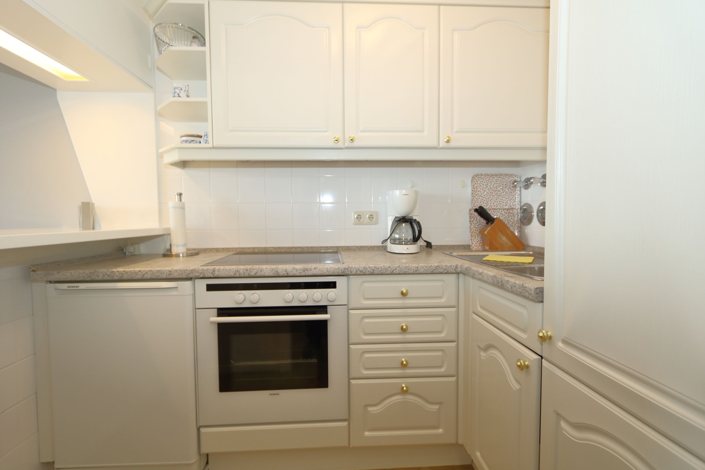 A compact kitchen with white cabinetry, a built-in oven, and a coffee maker.
