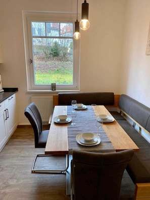 Un coin repas avec une table en bois dressée pour quatre personnes, un banc le long d’un des murs et une fenêtre donnant sur l’extérieur.
