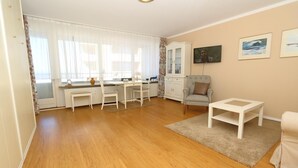 A living room with a wooden floor, a grey armchair, a white coffee table, and a cabinet with glass doors. - Haus am Meer14 - App. 109 WB (Sylt)
