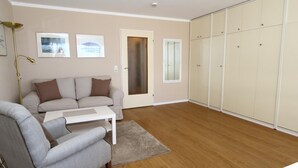 A living room with a sofa, armchair, and a coffee table. There is a wardrobe with sliding doors and a door with a frosted glass panel. - Haus am Meer14 - App. 109 WB (Sylt)