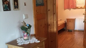 Un aparador de madera con un mantel de encaje, un collage de fotos en la pared y una puerta que da a un dormitorio con cama y mesita de noche.