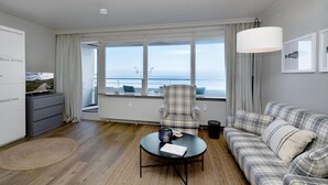 Ett modernt vardagsrum med ett stort fönster, en soffa med rutigt tyg, en fåtölj, ett litet bord och ett vitt skåp.