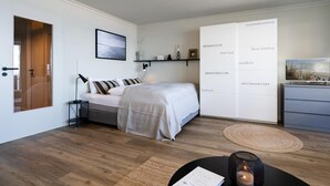 Ett modernt sovrum med en säng, ett sängbord, en lampa och en stor garderob.