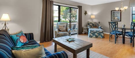 Un salon comprenant un canapé, une table basse, une table à manger avec des chaises, et une vue sur l’extérieur à travers une porte vitrée.