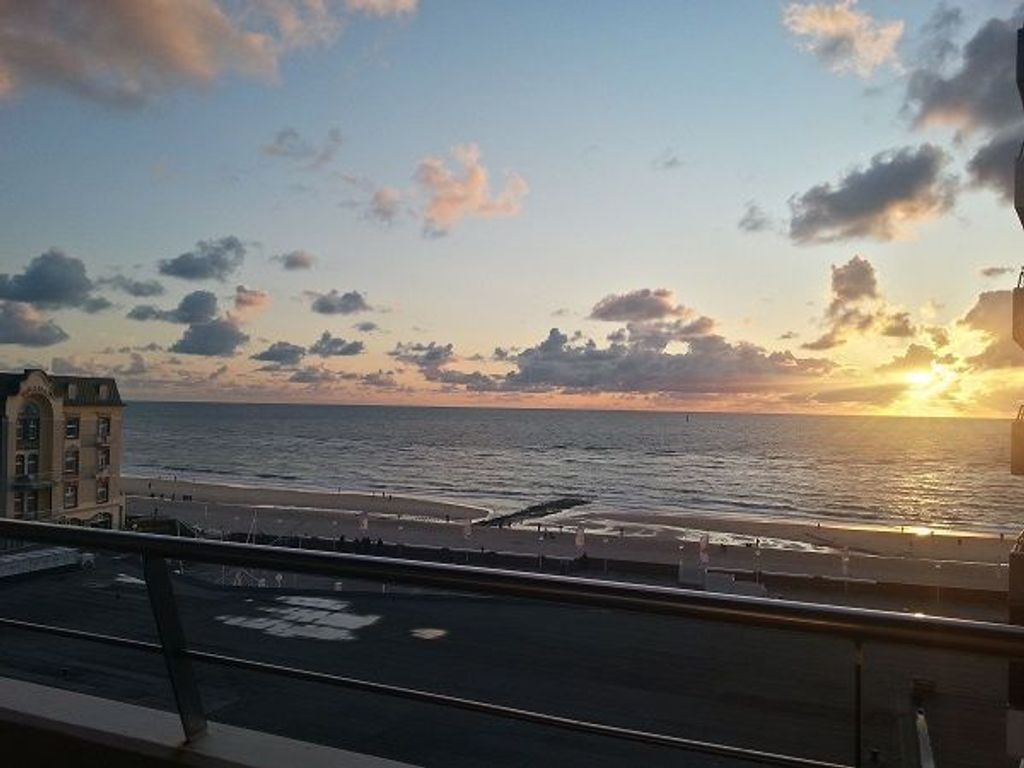 Ein Sonnenuntergangsblick von einem Balkon mit Blick auf einen Strand, im Vordergrund ein Gebäude.
