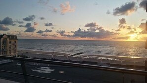 Solnedgangsudsig fra en balkon over et strandlandskab, med en bygning i forgrunden.
