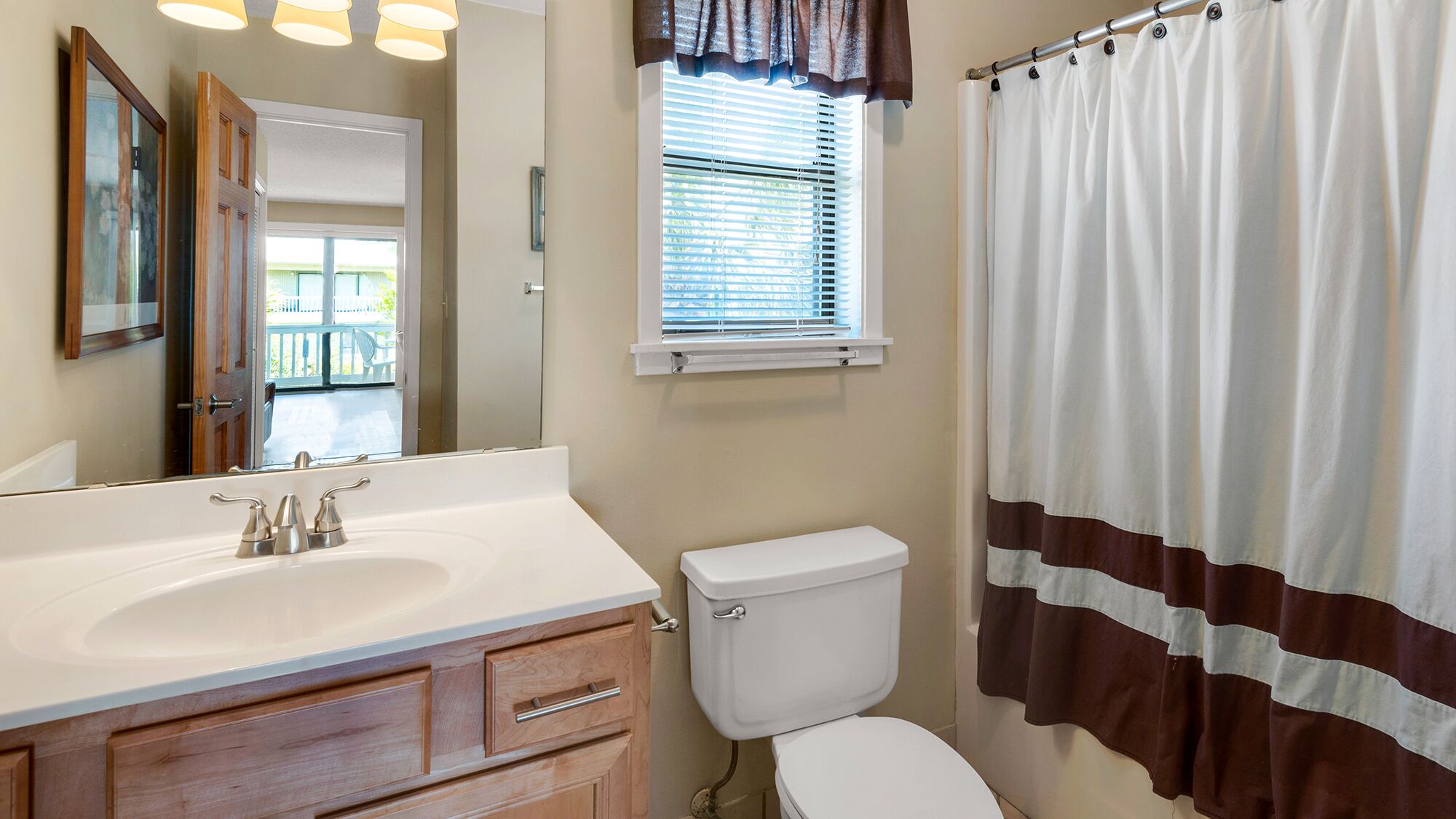 A bathroom with a white sink, wooden vanity, a toilet, and a shower curtain.