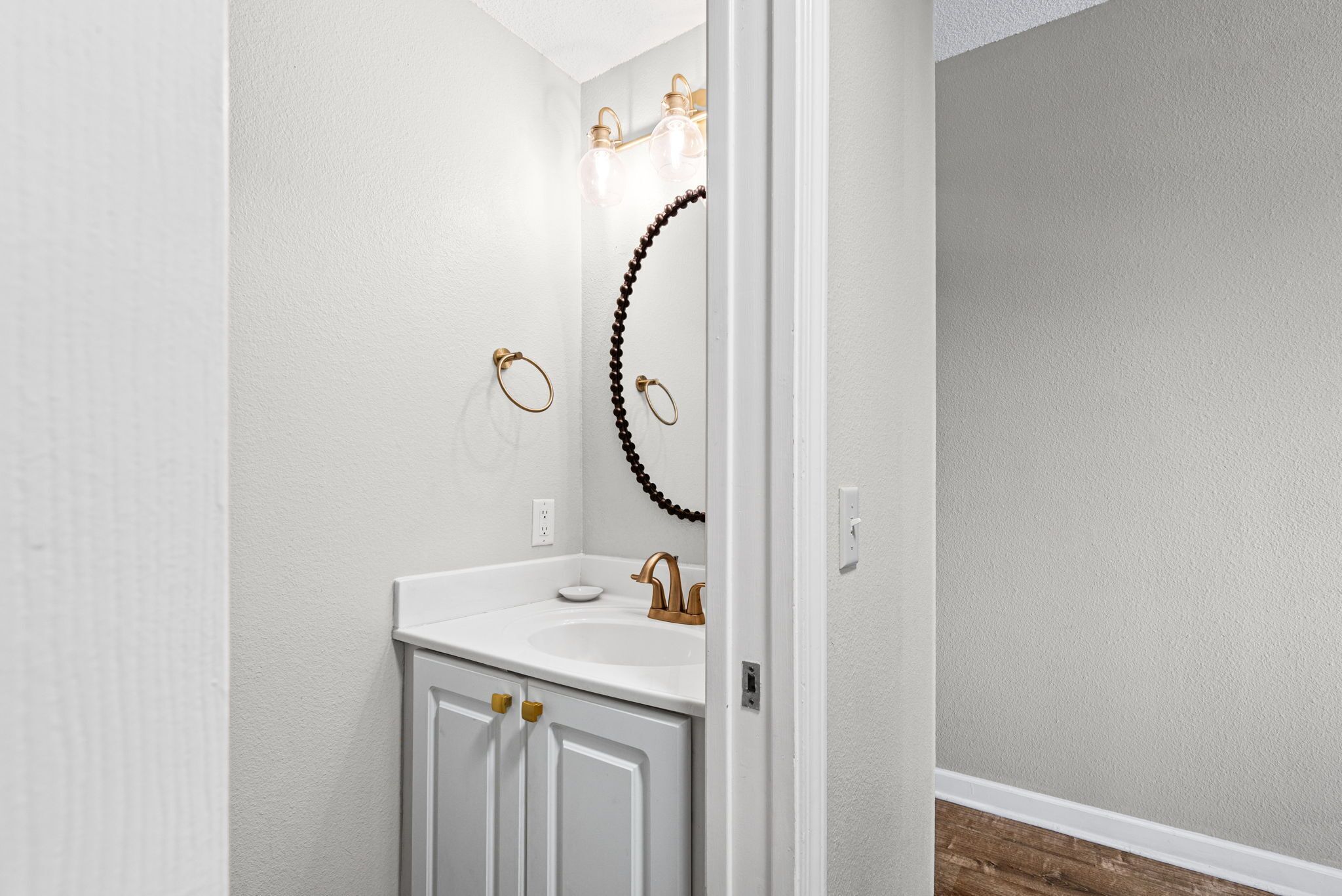Une salle de bain avec un meuble-lavabo blanc, un miroir et un luminaire placé au-dessus du miroir.